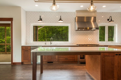 Example of a large trendy dark wood floor and brown floor kitchen design in Cedar Rapids with an undermount sink, shaker cabinets, medium tone wood cabinets, quartzite countertops, white backsplash, subway tile backsplash, stainless steel appliances and an island