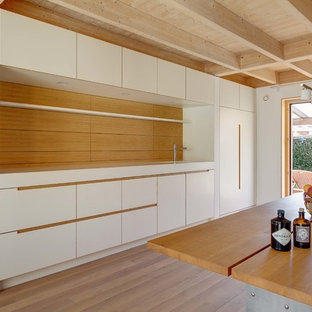 Ejemplo de cocina comedor lineal, escandinava, pequeña, con armarios con paneles lisos, puertas de armario blancas, encimera de acrílico, electrodomésticos negros y suelo de madera clara