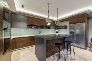 This is an example of a mid-sized industrial u-shaped eat-in kitchen in Sydney with an integrated sink, flat-panel cabinets, green cabinets, quartz benchtops, green splashback, glass sheet splashback, stainless steel appliances, limestone floors and with island.
