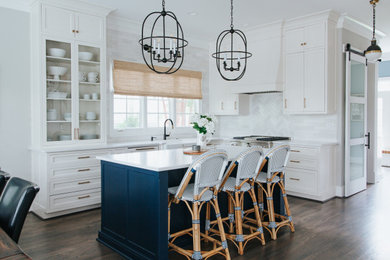Example of a mid-sized beach style l-shaped medium tone wood floor and brown floor kitchen pantry design in St Louis with a farmhouse sink, shaker cabinets, quartz countertops, white backsplash, marble backsplash, white appliances, an island, white countertops and blue cabinets
