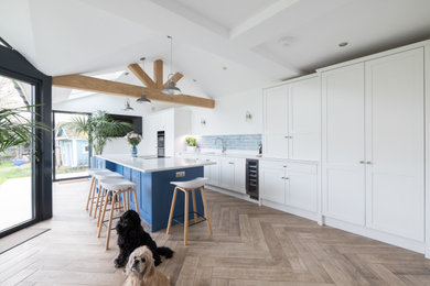 Design ideas for a large classic open plan kitchen in Cardiff with a submerged sink, shaker cabinets, light wood cabinets, quartz worktops, blue splashback, ceramic splashback, stainless steel appliances, porcelain flooring, an island, brown floors, white worktops and exposed beams.