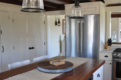 Photo of a mid-sized beach style l-shaped separate kitchen in Providence with a farmhouse sink, recessed-panel cabinets, white cabinets, granite benchtops, grey splashback, timber splashback, stainless steel appliances, medium hardwood floors, with island and beige floor.