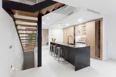 Photo of a modern single-wall kitchen in Other with flat-panel cabinets, with island, black benchtop, a single-bowl sink, light wood cabinets and white floor.
