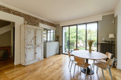 This is an example of a large contemporary open plan games room in Paris with grey walls, light hardwood flooring, no fireplace, a freestanding tv, beige floors and brick walls.