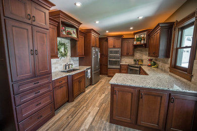 Example of a mid-sized classic u-shaped medium tone wood floor and beige floor kitchen design in Wichita with a drop-in sink, raised-panel cabinets, dark wood cabinets, granite countertops, beige backsplash, ceramic backsplash, stainless steel appliances and a peninsula