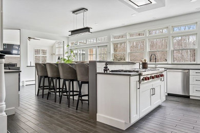 Transitional porcelain tile kitchen photo in Providence with a farmhouse sink, shaker cabinets, white cabinets, quartz countertops, white backsplash, subway tile backsplash, stainless steel appliances and an island