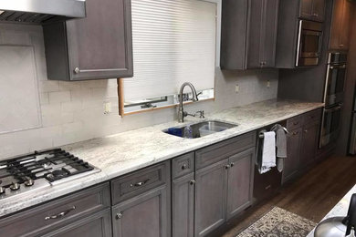 Example of a mid-sized minimalist dark wood floor and brown floor kitchen design in New York with a double-bowl sink, recessed-panel cabinets, dark wood cabinets, granite countertops, gray backsplash, subway tile backsplash, stainless steel appliances, an island and white countertops