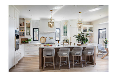 Photo of a large traditional l-shaped kitchen/diner in Other with a belfast sink, recessed-panel cabinets, quartz worktops, multi-coloured splashback, mosaic tiled splashback, light hardwood flooring, an island, brown floors, white worktops and a wallpapered ceiling.