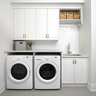 Photo of a traditional single-wall utility room in Toronto with a submerged sink, raised-panel cabinets, white cabinets, white walls, a side by side washer and dryer and grey worktops.