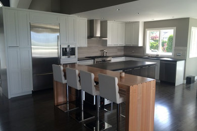 Mid-sized minimalist l-shaped dark wood floor and brown floor open concept kitchen photo in Vancouver with an undermount sink, shaker cabinets, white cabinets, solid surface countertops, beige backsplash, ceramic backsplash, stainless steel appliances and two islands