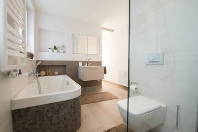Geräumiges Modernes Badezimmer En Suite mit Einbaubadewanne, bodengleicher Dusche, Wandtoilette, Wandwaschbecken, flächenbündigen Schrankfronten, beigen Schränken, weißer Wandfarbe und hellem Holzboden in Dortmund
