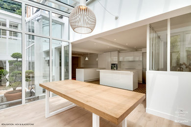 Large contemporary kitchen/dining combo in Paris with light hardwood floors and white walls.