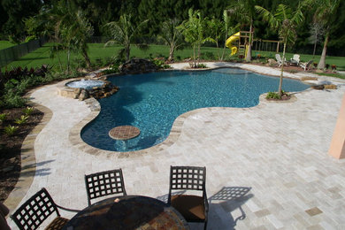 Example of an island style backyard brick and custom-shaped pool design in Miami