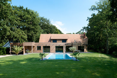 Réalisation d'une grande façade de maison marron design en bois à un étage avec un toit à croupette et un toit en tuile.