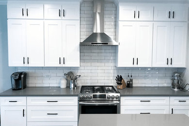 Example of a large transitional u-shaped dark wood floor and brown floor eat-in kitchen design in Chicago with a farmhouse sink, shaker cabinets, white cabinets, quartz countertops, white backsplash, ceramic backsplash, stainless steel appliances, an island and gray countertops