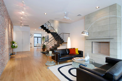 This is an example of a large modern loft-style living room in New York with white walls, light hardwood floors and a concrete fireplace surround.