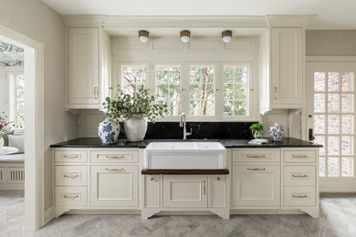 Mid-sized elegant limestone floor and beige floor enclosed kitchen photo in Minneapolis with a farmhouse sink, recessed-panel cabinets, white cabinets, soapstone countertops, black backsplash, stone slab backsplash, paneled appliances, an island and black countertops