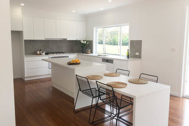 Design ideas for a large modern galley open plan kitchen in Wollongong with a built-in sink, flat-panel cabinets, white cabinets, composite countertops, grey splashback, ceramic splashback, stainless steel appliances, bamboo flooring, an island and multi-coloured floors.
