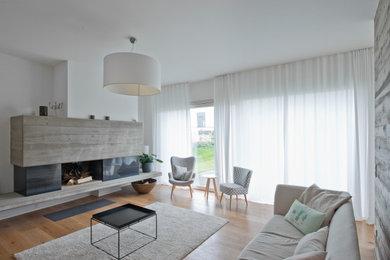 Mittelgroßes, Offenes Modernes Wohnzimmer mit weißer Wandfarbe, hellem Holzboden, Hängekamin und Kaminumrandung aus Beton in Leipzig
