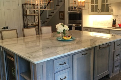 This is an example of a large traditional u-shaped kitchen in Nashville with a farmhouse sink, shaker cabinets, white cabinets, granite benchtops, white splashback, stone tile splashback, stainless steel appliances, porcelain floors and with island.