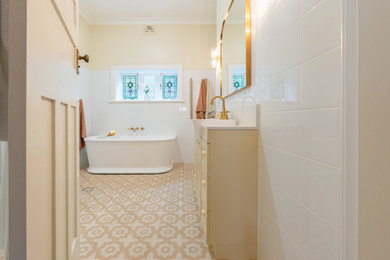 This is an example of a large traditional bathroom in Sydney with shaker cabinets, yellow cabinets, a freestanding tub, a corner shower, a two-piece toilet, white tile, yellow walls, porcelain floors, a drop-in sink, multi-coloured floor, a hinged shower door, beige benchtops, a single vanity and a freestanding vanity.