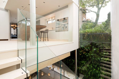 Large modern single-wall open plan kitchen in London with a built-in sink, white cabinets, white splashback, stainless steel appliances, terrazzo flooring, an island and white floors.