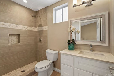 Example of a mid-sized master brown tile and porcelain tile porcelain tile and brown floor doorless shower design in Orange County with shaker cabinets, white cabinets, a two-piece toilet, gray walls, an undermount sink and quartz countertops