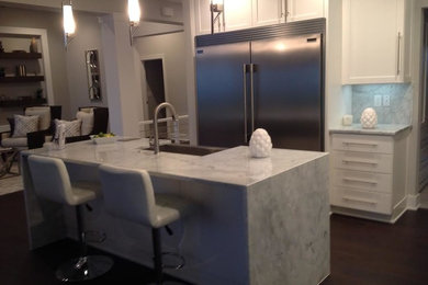 Inspiration for a mid-sized transitional single-wall dark wood floor and brown floor open concept kitchen remodel in Other with a farmhouse sink, shaker cabinets, white cabinets, marble countertops, white backsplash, stone slab backsplash, stainless steel appliances and an island