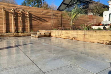 This is an example of a large mediterranean back partial sun garden for summer in Surrey with a raised bed, natural stone paving and a wood fence.