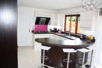 Mid-sized contemporary u-shaped kitchen in Belfast with a single-bowl sink, flat-panel cabinets, beige cabinets, laminate benchtops, pink splashback, glass sheet splashback, ceramic floors and no island.