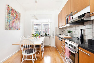 Photo of a transitional single-wall eat-in kitchen in Malmo with flat-panel cabinets, light wood cabinets, beige splashback, stainless steel appliances, light hardwood floors, no island and laminate benchtops.