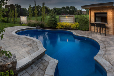 Photo of a mid-sized traditional backyard custom-shaped natural pool in Toronto with a pool house and natural stone pavers.