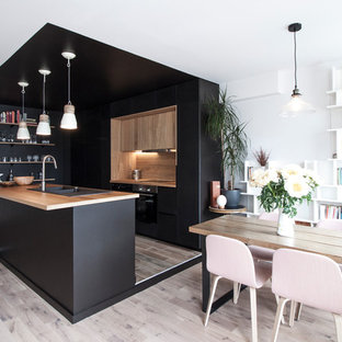 Diseño de cocina de galera, escandinava, de tamaño medio, abierta, con fregadero de doble seno, puertas de armario negras, encimera de madera, electrodomésticos negros, suelo de madera clara, una isla y salpicadero marrón