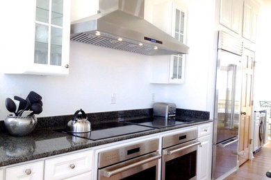 Mid-sized trendy u-shaped slate floor and brown floor eat-in kitchen photo in Little Rock with a double-bowl sink, flat-panel cabinets, white cabinets, white backsplash, stainless steel appliances, an island and black countertops