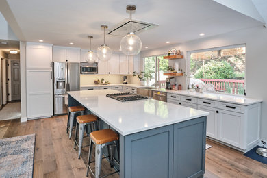 Example of a large transitional l-shaped medium tone wood floor and brown floor kitchen design in Seattle with a farmhouse sink, shaker cabinets, white cabinets, stainless steel appliances, an island and white countertops