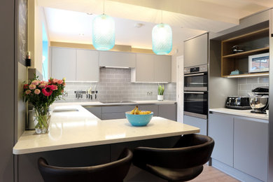This is an example of a large contemporary grey and teal u-shaped kitchen/diner in Hertfordshire with an integrated sink, flat-panel cabinets, grey cabinets, quartz worktops, grey splashback, metro tiled splashback, stainless steel appliances, lino flooring, a breakfast bar, brown floors, white worktops and feature lighting.