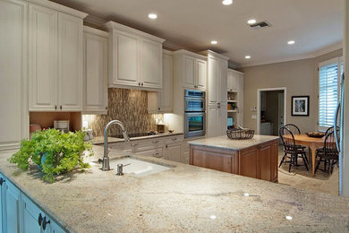 Example of a large classic l-shaped travertine floor eat-in kitchen design in Miami with an undermount sink, raised-panel cabinets, white cabinets, granite countertops, beige backsplash, glass tile backsplash, stainless steel appliances and an island