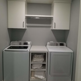 ダラスの小さいトランジショナルスタイルのおしゃれな洗濯室 (フラットパネル扉のキャビネット、白いキャビネット、ラミネートカウンター、グレーの壁、ラミネートの床、左右配置の洗濯機・乾燥機、茶色い床、白いキッチンカウンター) の写真