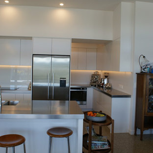 Large contemporary kitchen pantry designs - Inspiration for a large contemporary galley concrete floor kitchen pantry remodel in Dunedin with an integrated sink, flat-panel cabinets, white cabinets, stainless steel countertops, white backsplash, glass sheet backsplash, stainless steel appliances and an island