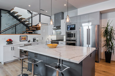 Kitchen - contemporary l-shaped medium tone wood floor and brown floor kitchen idea in Los Angeles with flat-panel cabinets, gray cabinets, stainless steel appliances, an island and white countertops
