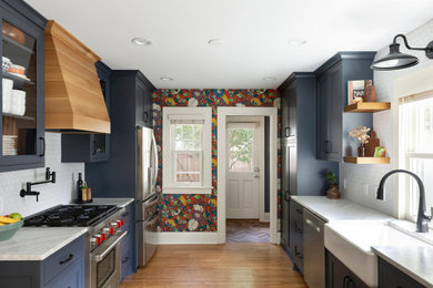 Inspiration for a mid-sized transitional galley medium tone wood floor and brown floor kitchen remodel in Minneapolis with a farmhouse sink, shaker cabinets, blue cabinets, marble countertops, white backsplash, ceramic backsplash, stainless steel appliances, white countertops and no island