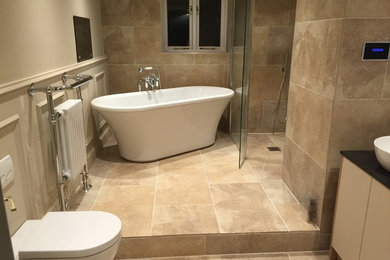 Photo of a large traditional kids bathroom in Other with raised-panel cabinets, beige cabinets, a freestanding tub, an open shower, a one-piece toilet, beige tile, porcelain tile, beige walls, porcelain floors, a vessel sink and granite benchtops.