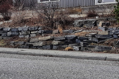 Design ideas for a mid-sized rustic full sun hillside stone retaining wall landscape in Calgary for winter.