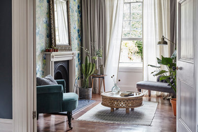 Inspiration for a medium sized eclectic living room feature wall in London with a reading nook, green walls, dark hardwood flooring, a standard fireplace, a wooden fireplace surround, no tv, brown floors and wallpapered walls.