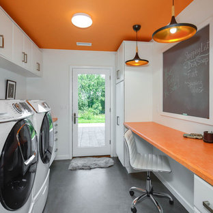プロビデンスの中サイズのインダストリアルスタイルのおしゃれな家事室 (スロップシンク、フラットパネル扉のキャビネット、白いキャビネット、ラミネートカウンター、オレンジの壁、コンクリートの床、左右配置の洗濯機・乾燥機、グレーの床、オレンジのキッチンカウンター) の写真