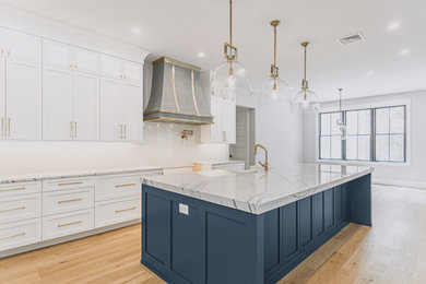 Example of a farmhouse light wood floor eat-in kitchen design in Philadelphia with a farmhouse sink, shaker cabinets, white cabinets, marble countertops, white backsplash, ceramic backsplash, stainless steel appliances, an island and white countertops