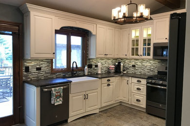Photo of a mid-sized mediterranean u-shaped eat-in kitchen in Chicago with a farmhouse sink, raised-panel cabinets, white cabinets, quartz benchtops, green splashback, glass tile splashback, stainless steel appliances, ceramic floors, no island, multi-coloured floor and brown benchtop.