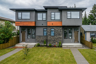 This is an example of a large contemporary two-storey stucco grey duplex exterior in Calgary with a flat roof and a metal roof.