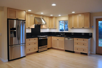 Open concept kitchen - modern l-shaped light wood floor and white floor open concept kitchen idea in Other with an undermount sink, shaker cabinets, light wood cabinets, solid surface countertops, black backsplash, stainless steel appliances, no island and black countertops