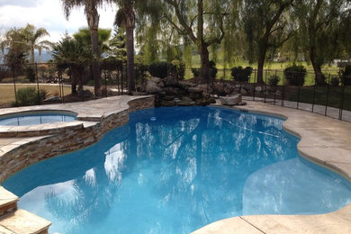 Large tropical backyard custom-shaped pool in Orange County with a hot tub and stamped concrete.